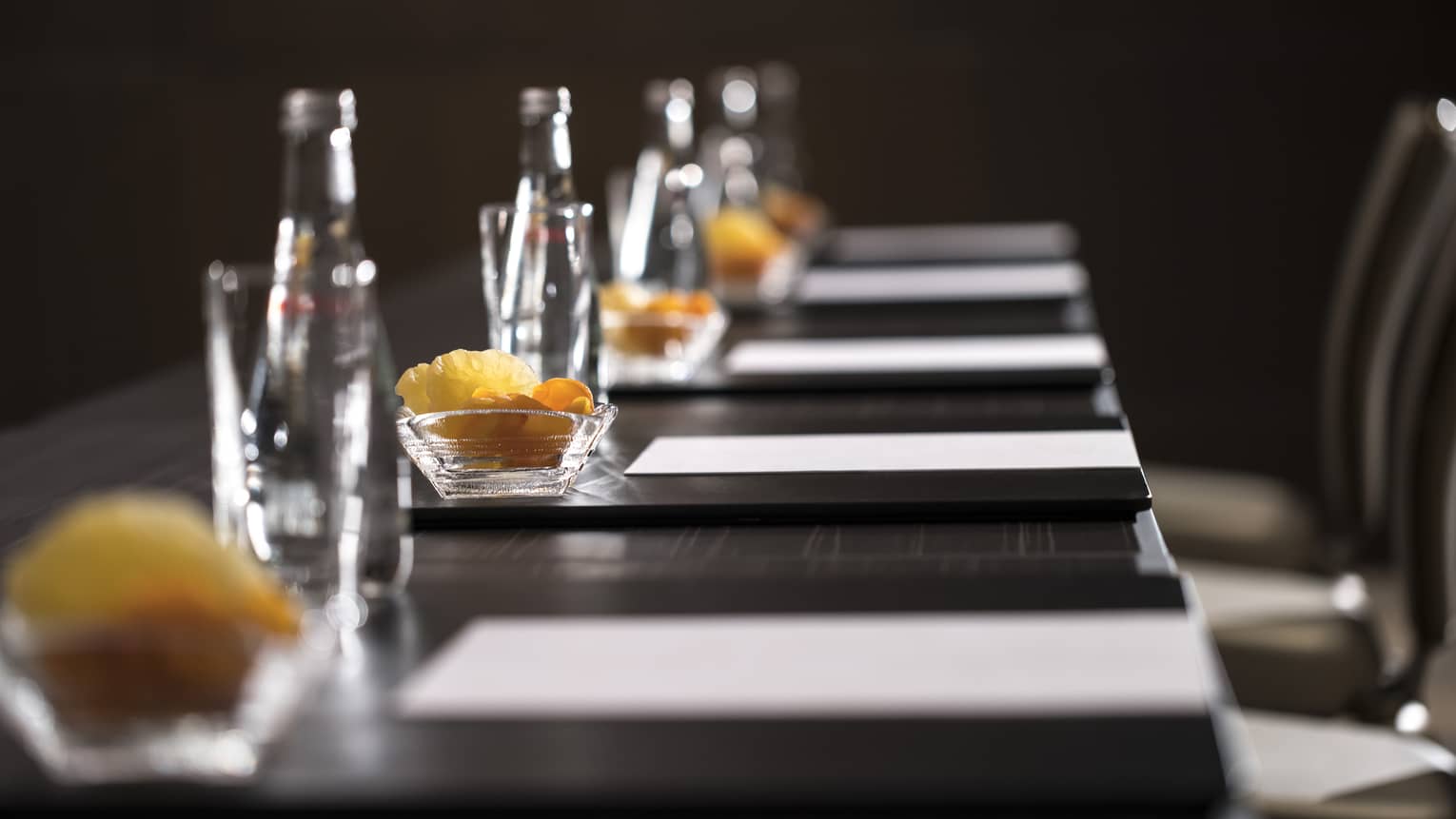 Row of glass bottles, small dishes with dried fruits, meeting agendas along boardroom table