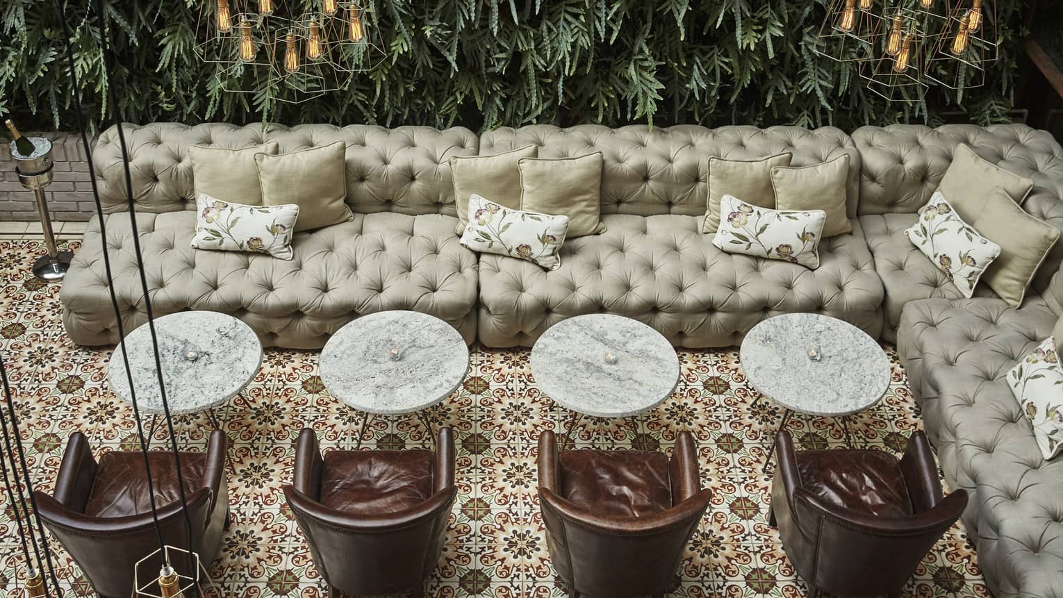 Aerial view past hanging lamps to lounge with large tufted leather sofas, cocktail tables and chairs, tile floor