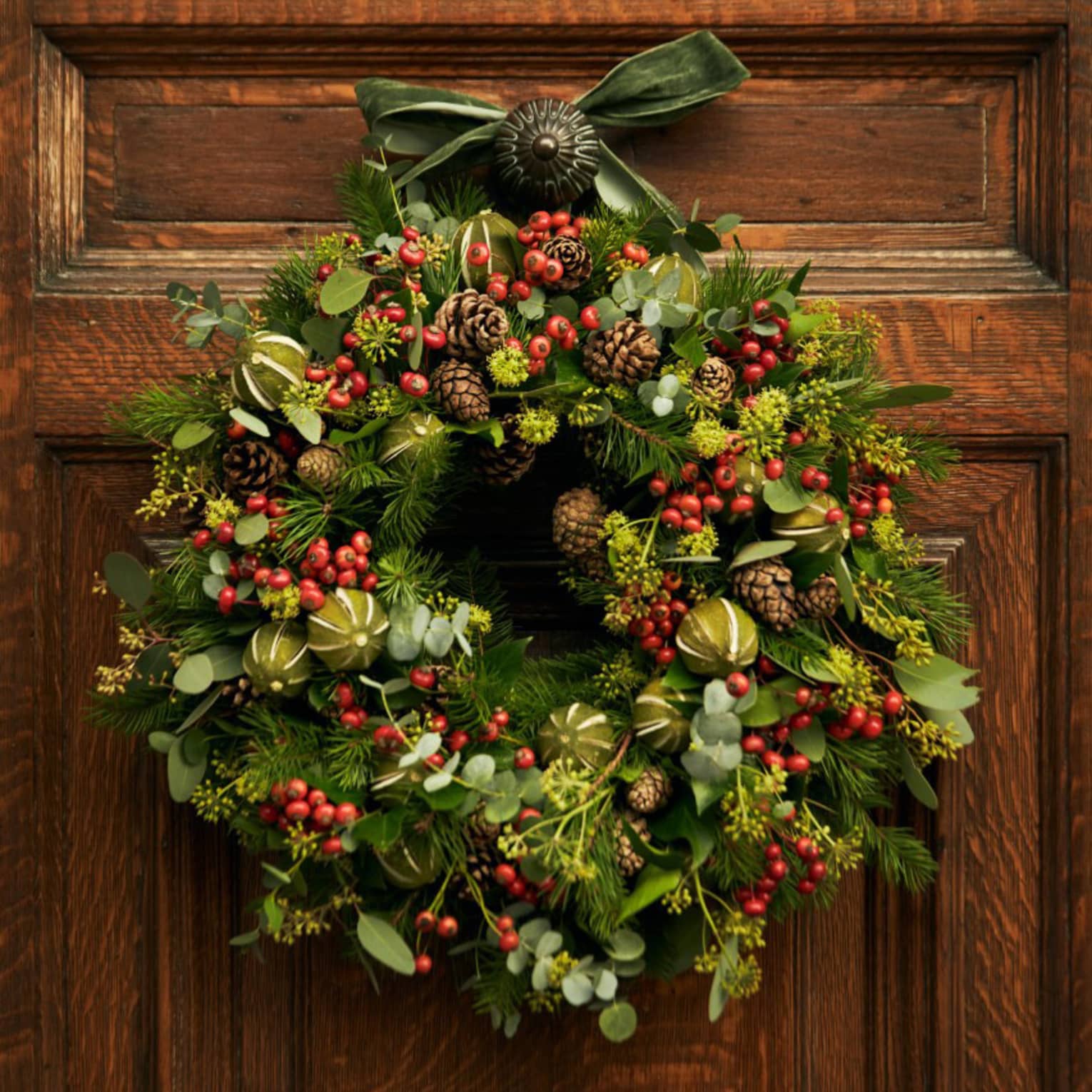 A wreath with red berries hanging on a wood door.