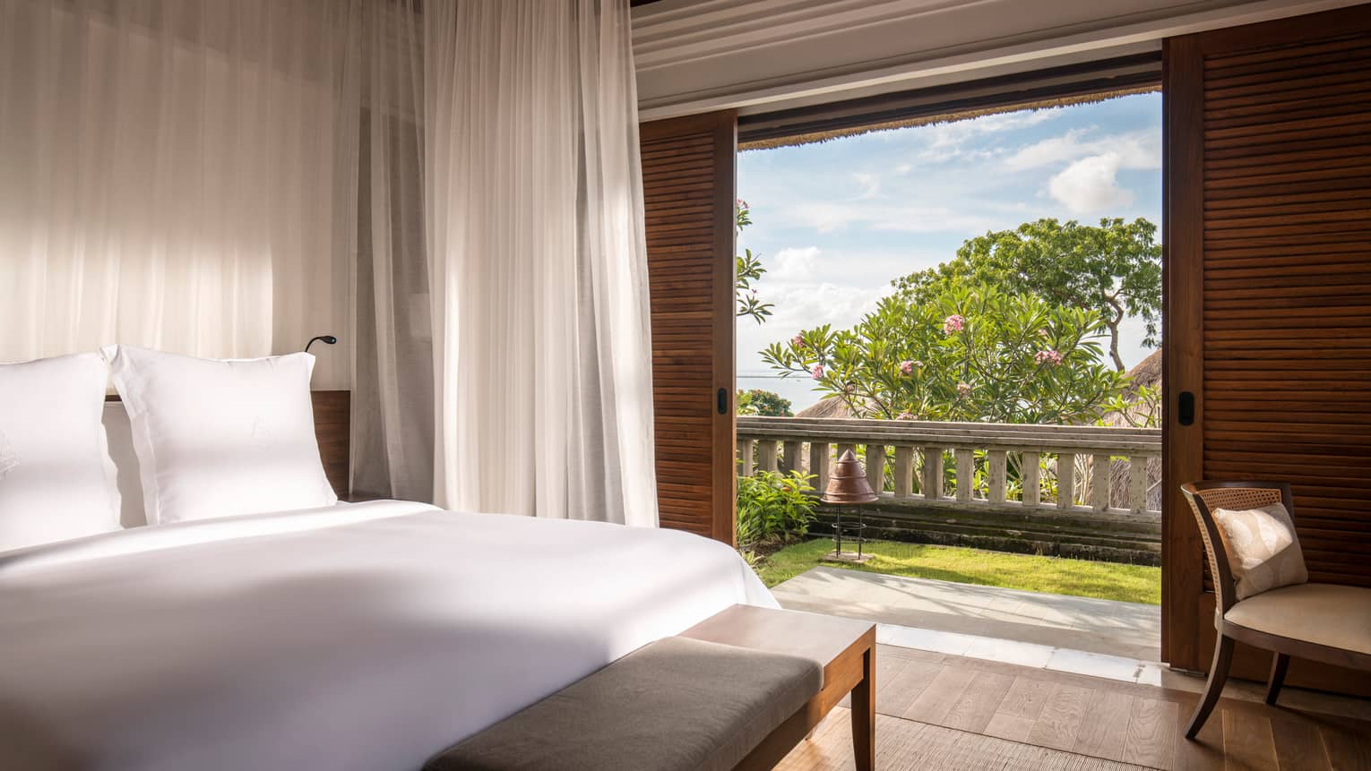 Sunny Garden Villa bedroom with bed with white linens, open patio door to grass, wood railing