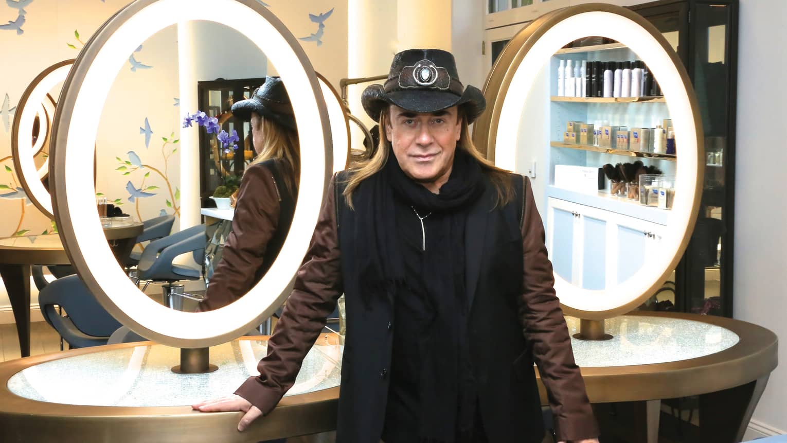 Portrait photo of stylist José Eber wearing hat in front of vanity, mirrors
