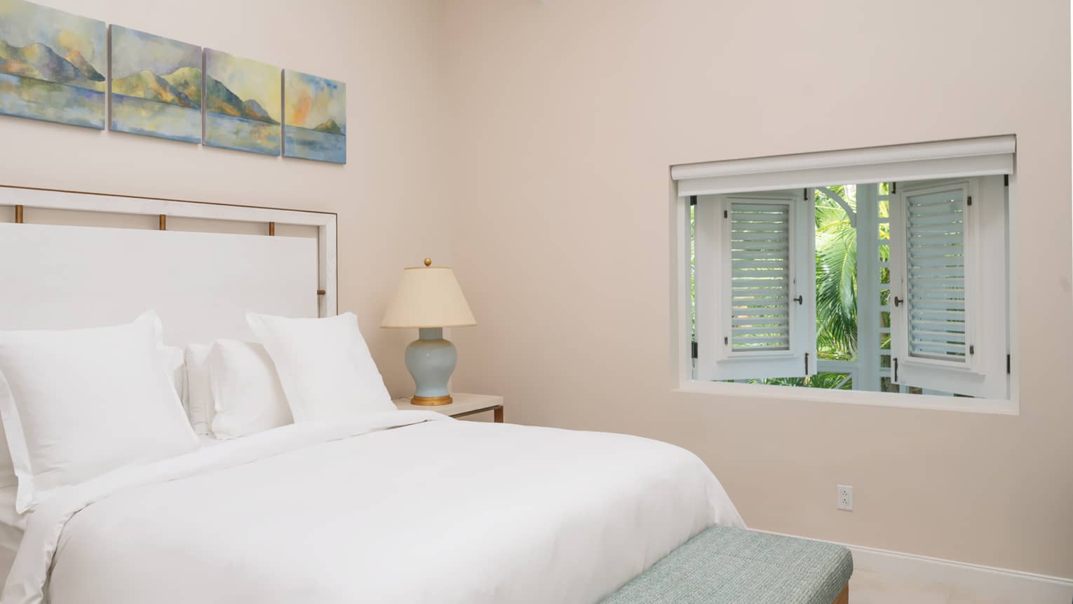 Bedroom with white king bed, white headboard, pale pink walls and white shuttered window