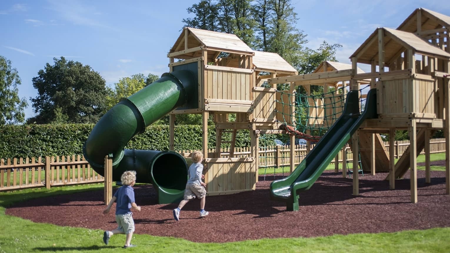 Two young children running towards a playgrounds on a sunny day outside.