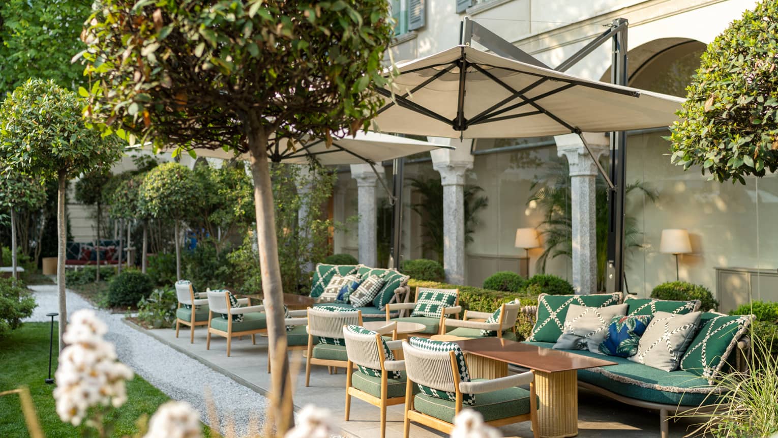 An outdoor seating area with umbrellas and green chairs surrounded by small trees.