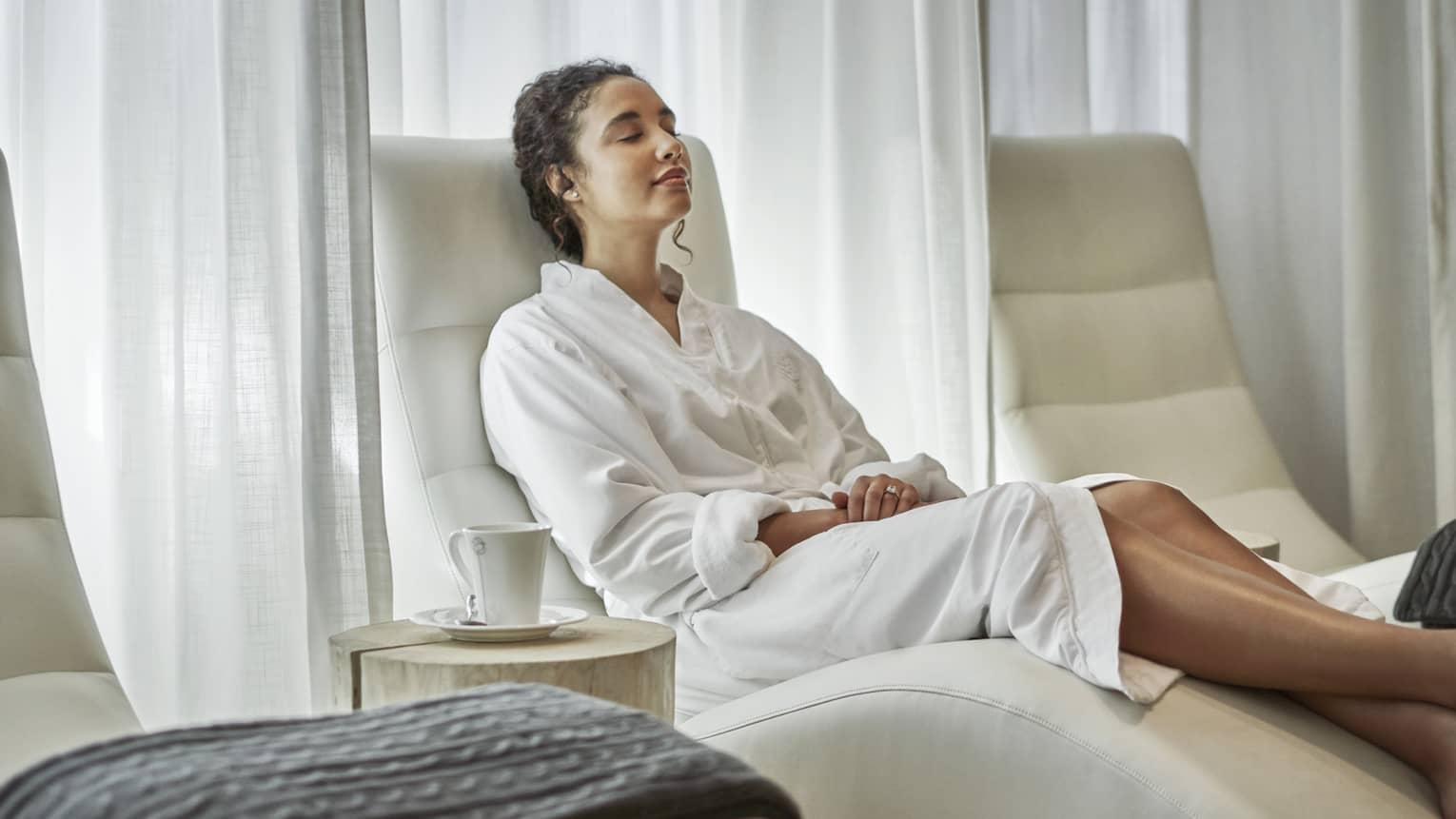 A woman in a white robe lounges on a curved chair after a spa treatment.