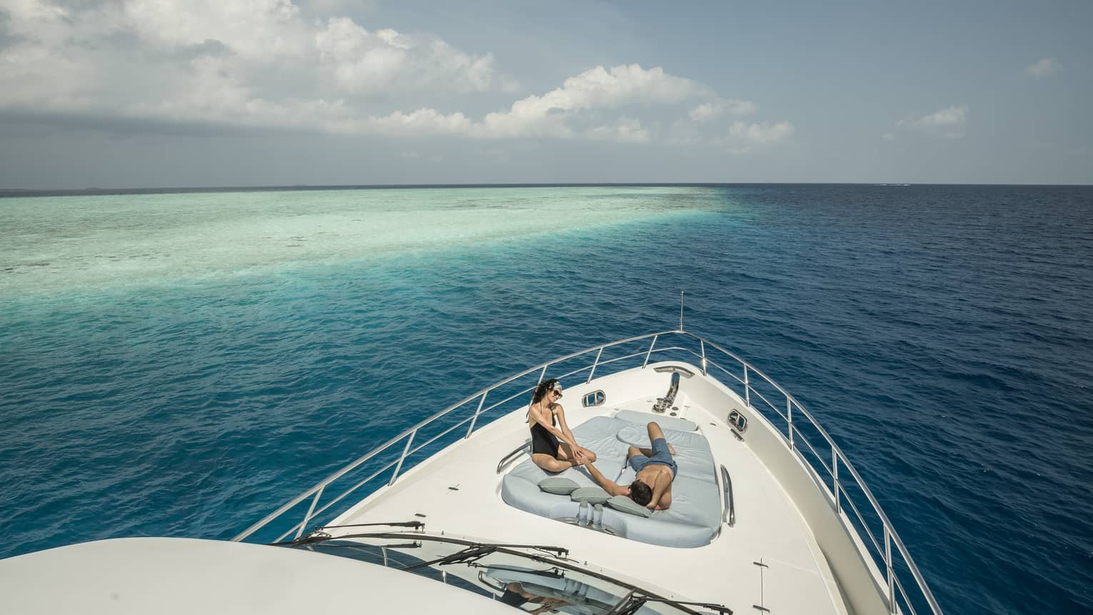 Couple lounge on cushions at front of private yacht on ocean