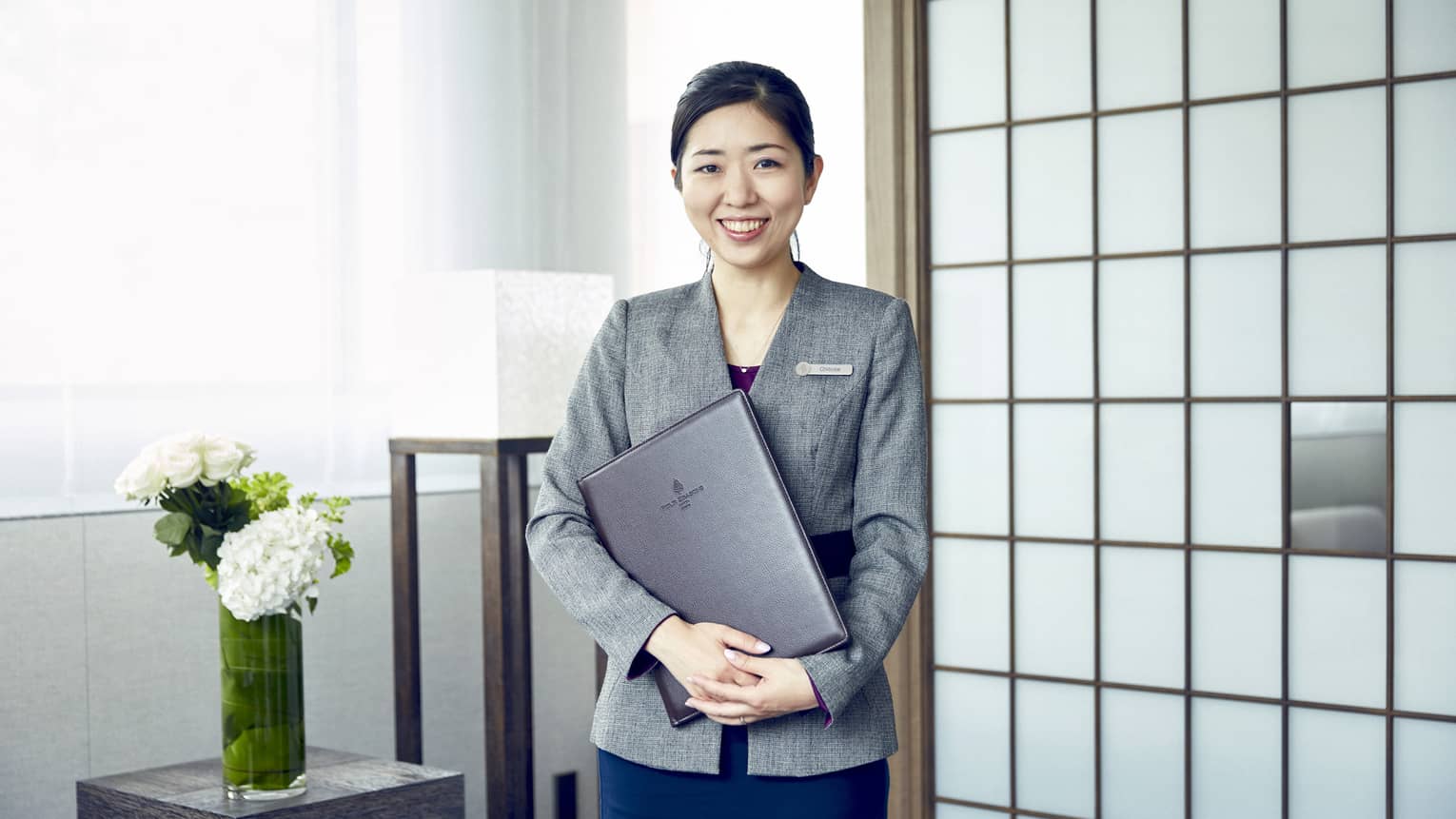 Portrait photo of smiling wedding consultant holding binder against wall