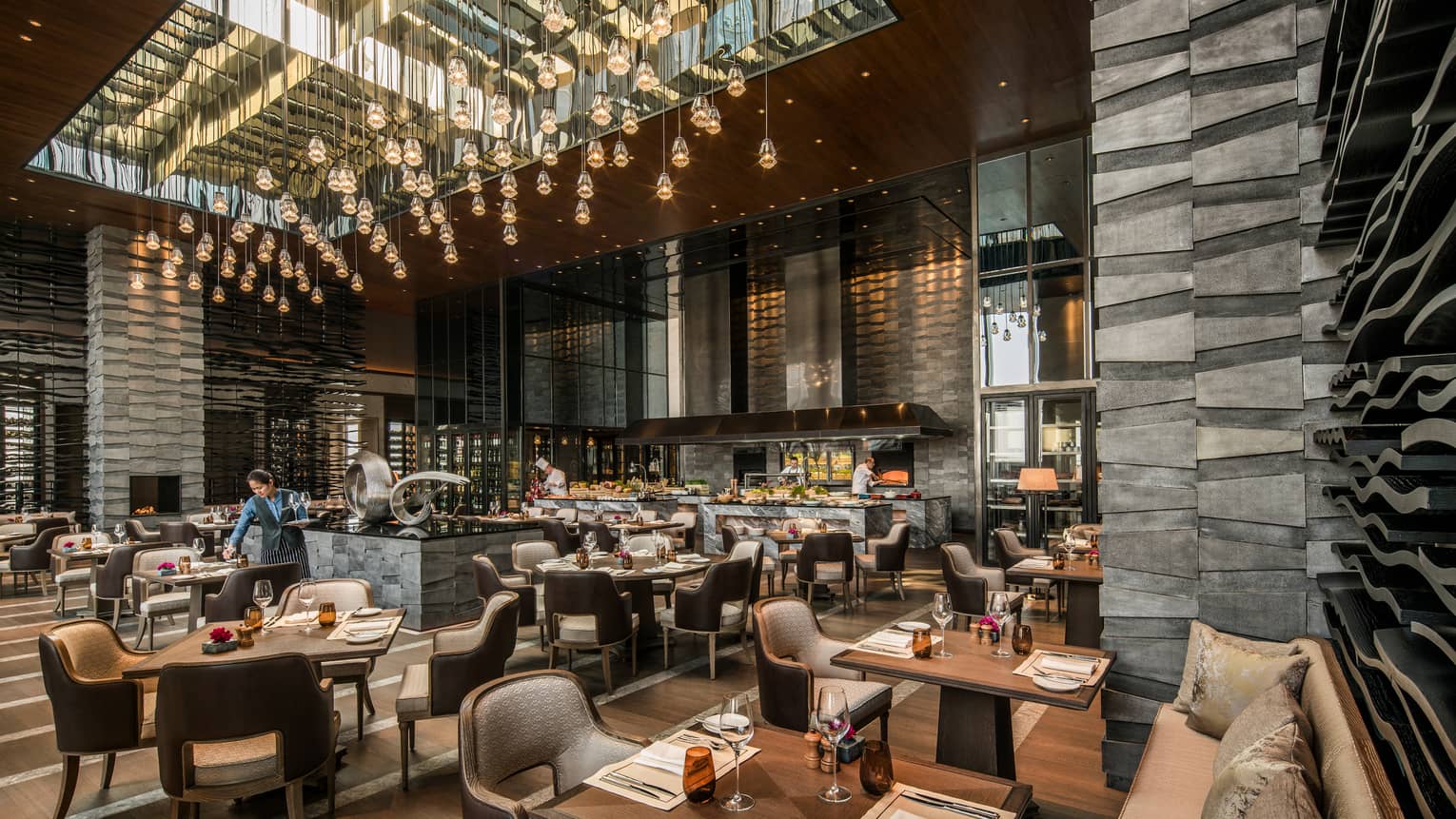 Server sets table in large Cielo dining room under hanging strings with crystal lights
