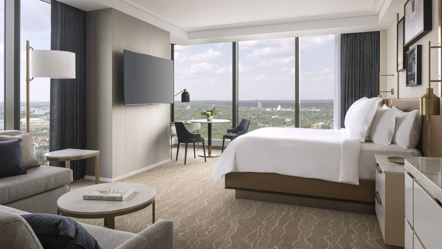 Hotel room with king bed, sofa, wall-mounted TV and wall of windows