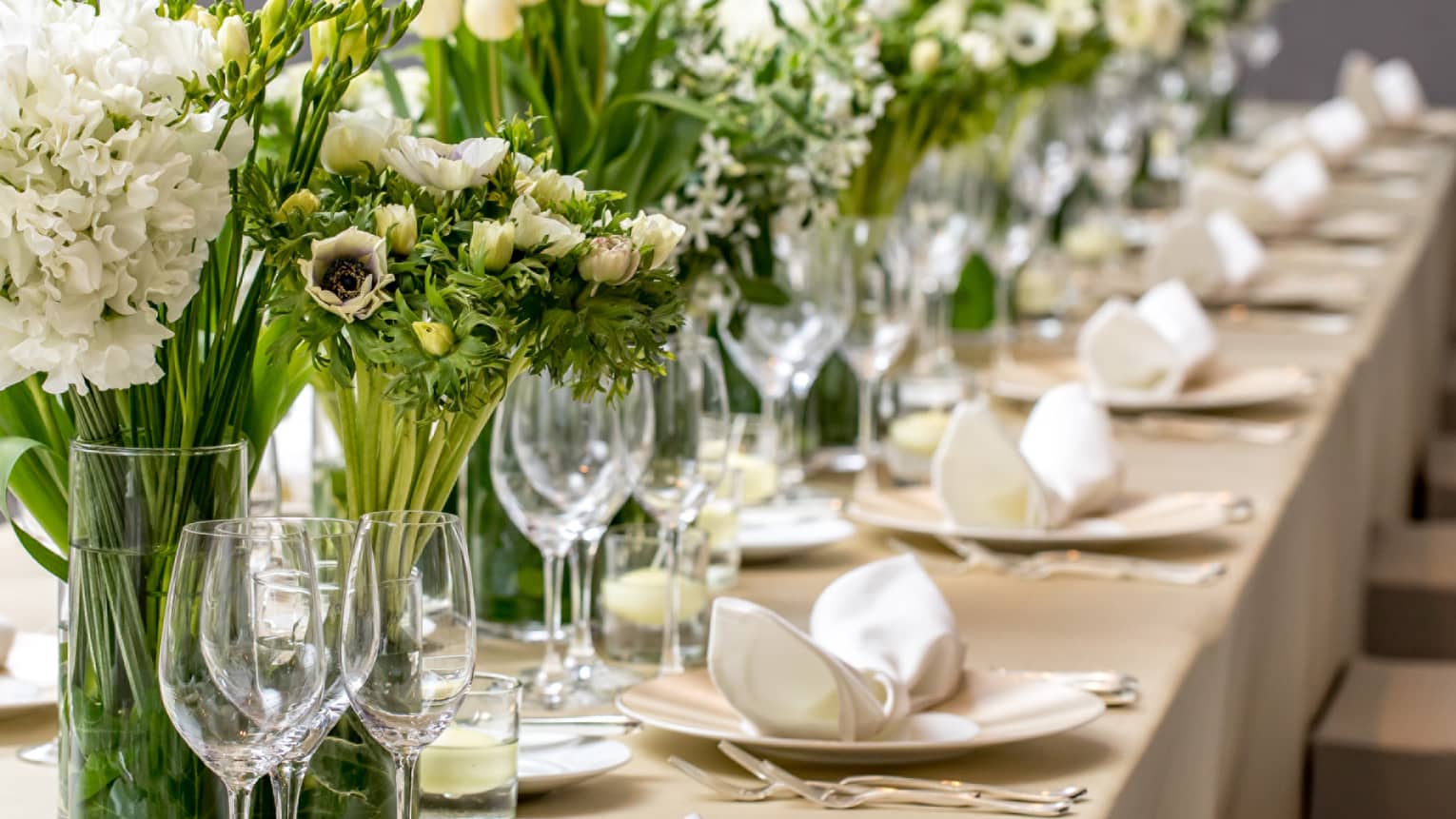 Close-up of long wedding dining table with wine glasses, white flowers in vases 