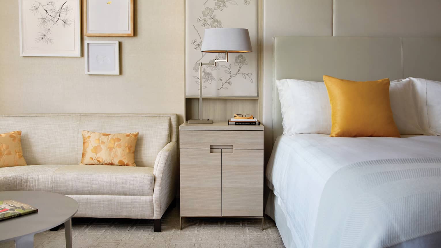 White loveseat by light wood nightstand, bed with golden yellow accent pillow