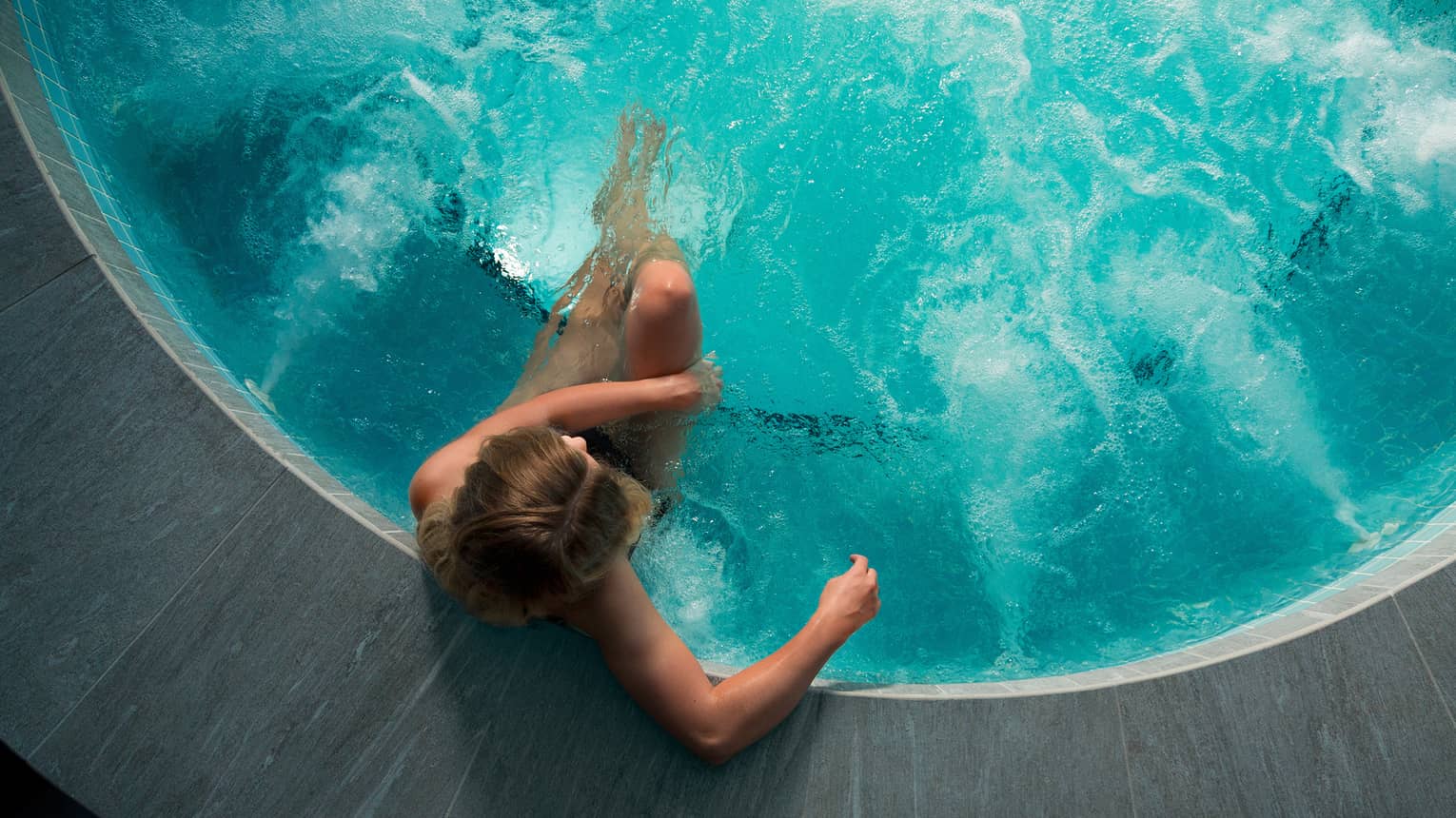 Looking down at woman sitting in round hot tub with blue water