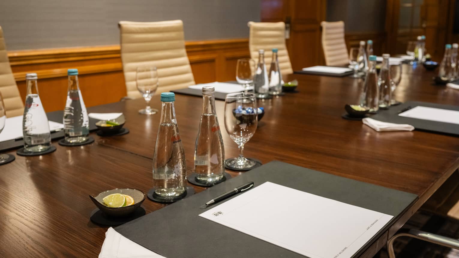 A meeting room with a table set with pens, paper, water and glasses