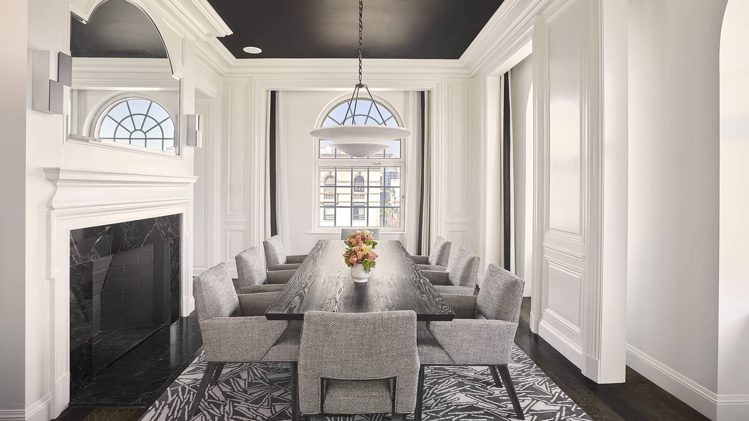Dining room with fireplace, arched window, and dark wood table with eight grey cushioned chairs