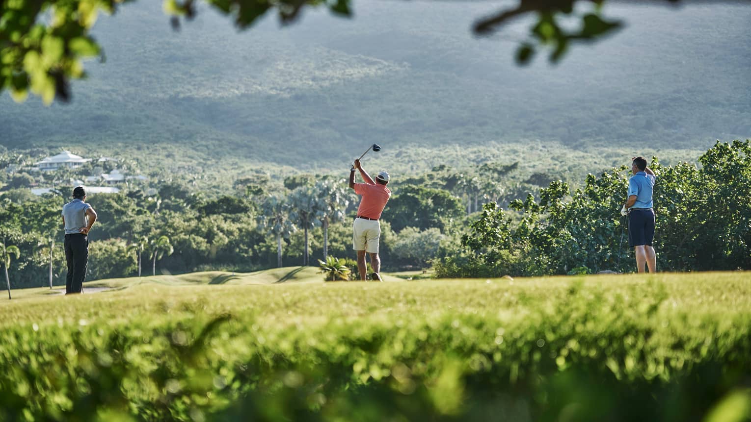 Back of three people standing on Robert Trent Jones II Golf Course, man swings golf club