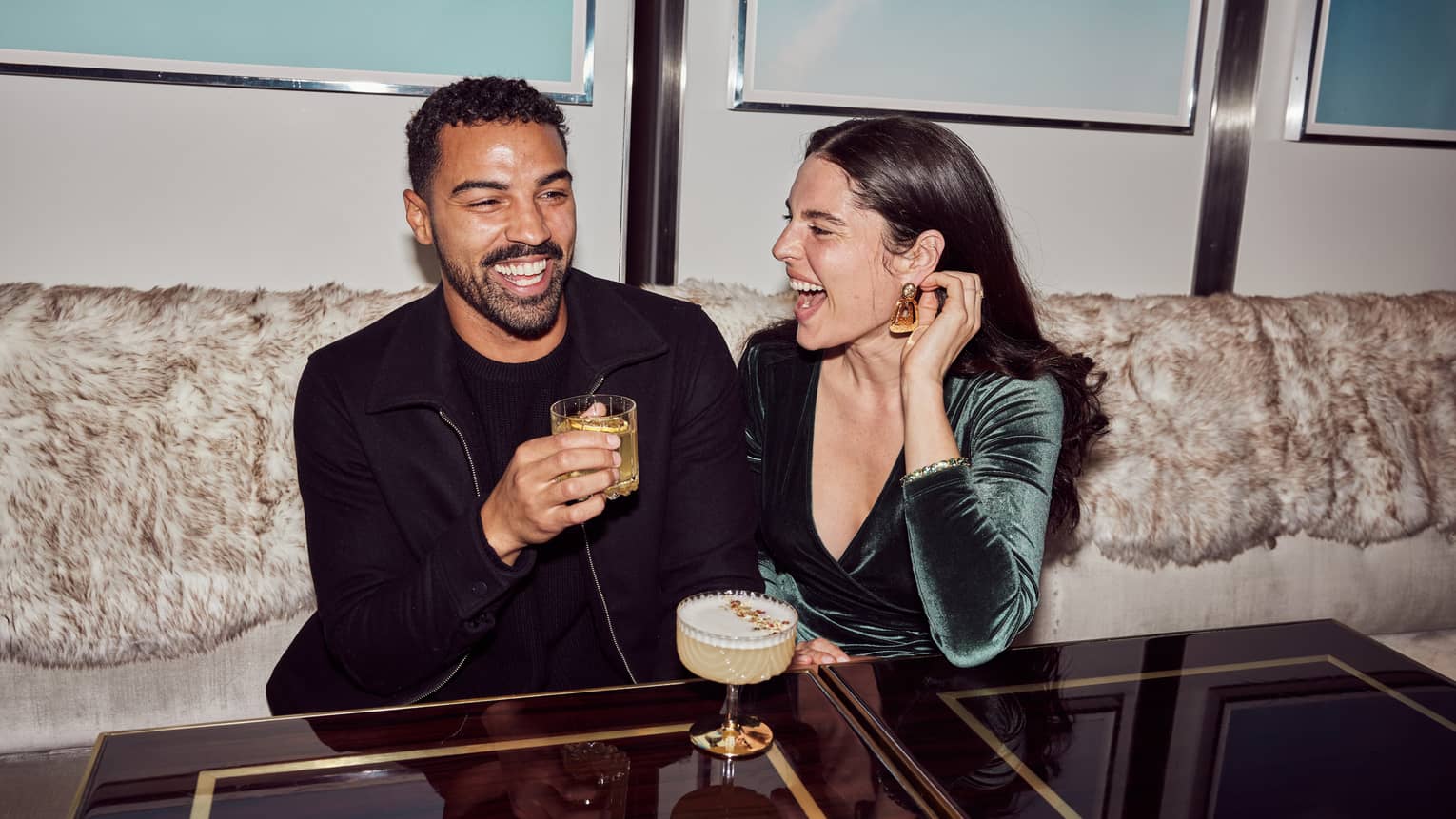 A couple laughs while enjoying cocktails in a booth