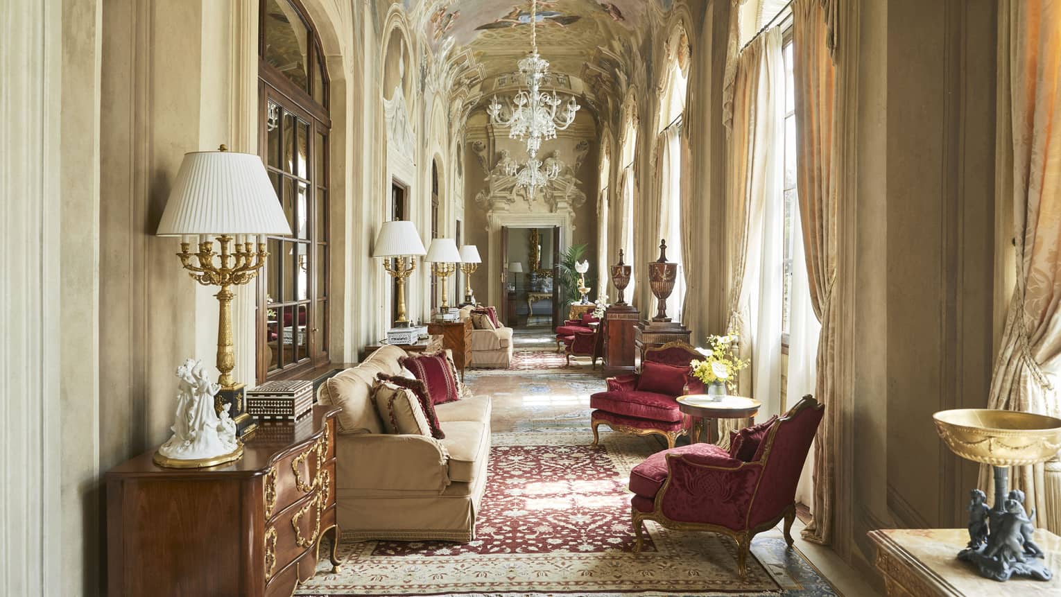 Grand, arched hallway with frescoed ceiling and chandelier, lounge seating and ruby-red arm chairs, in the Royal Suite at Four Seasons Hotel Florence