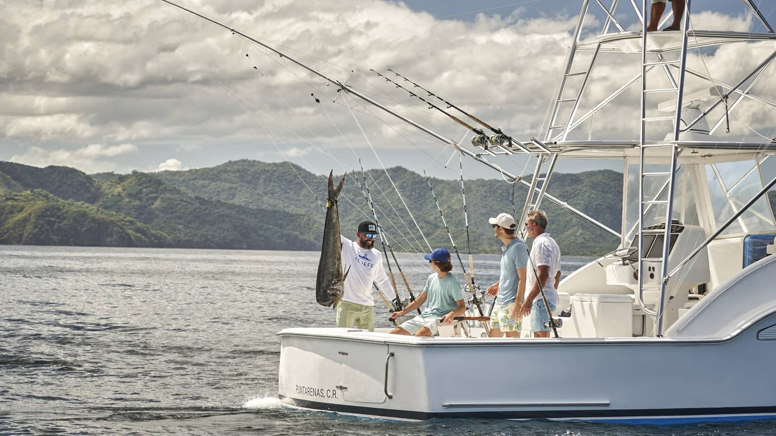 Four men are gathered on the back of a fishing boat with one of them holding a large fish up by the tail