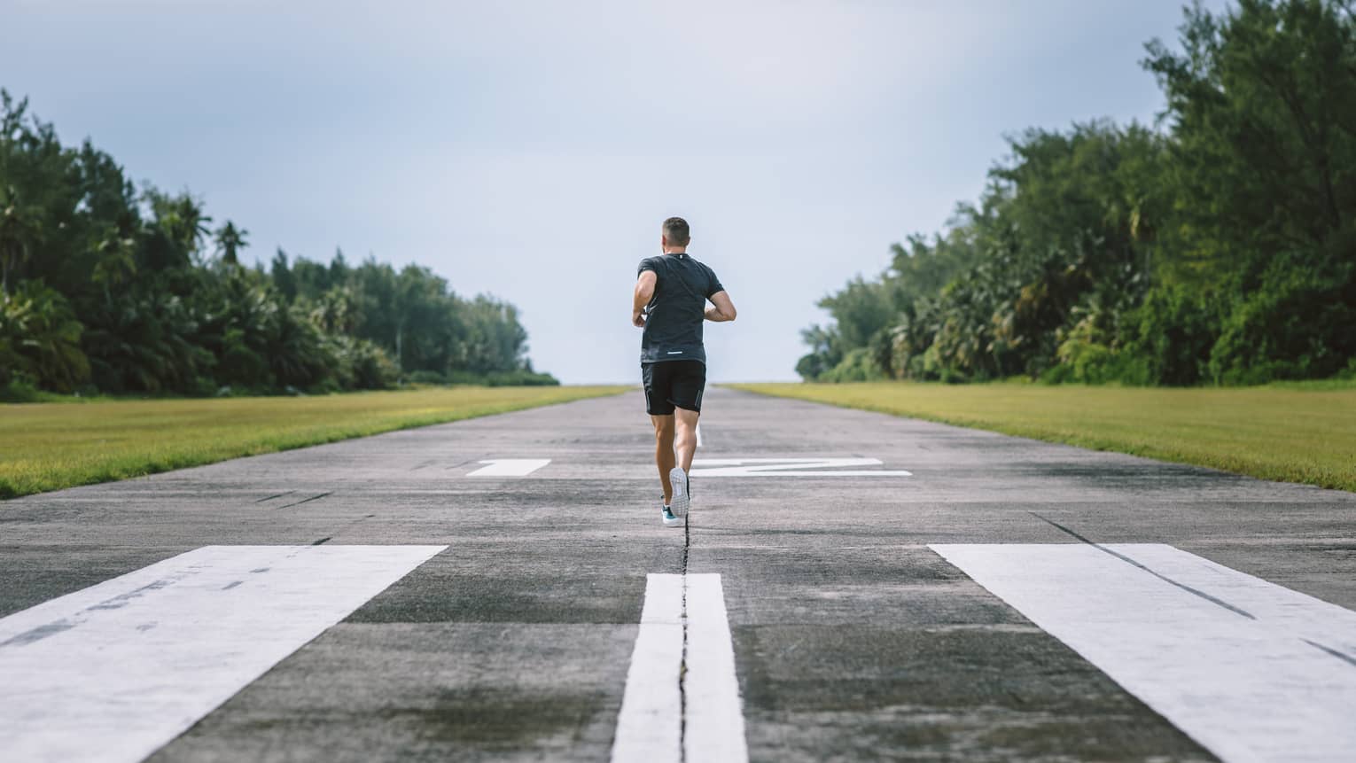 Man runs down airport runway with palm trees on either side