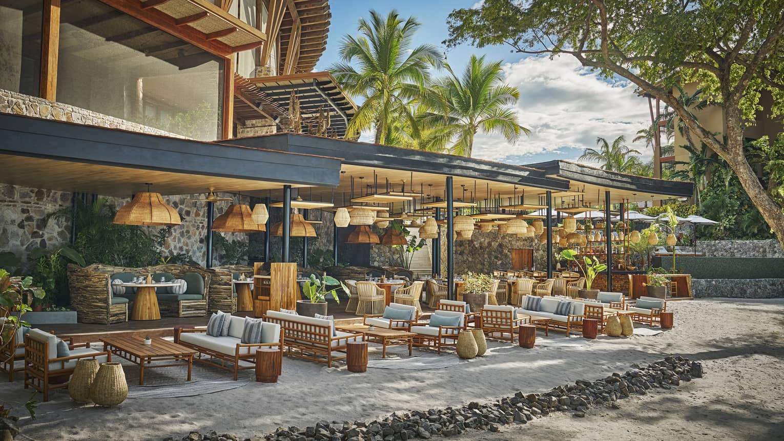 Tables, chairs and lounge seating set in groups on the sand along the edge of a reestaurant terrace
