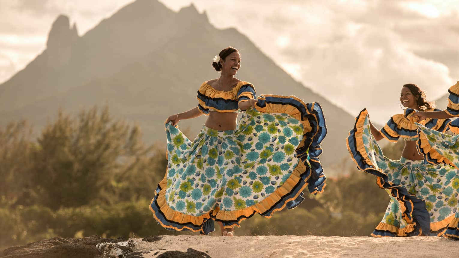 Zilwa Night Sega dancer twirls in colourful dress on sand in front of mountain, sunset