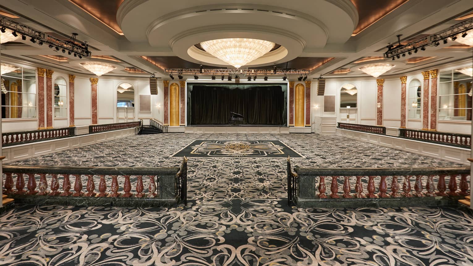 Spacious, empty, carpeted ballroom under large dome ceiling, crystal chandelier 