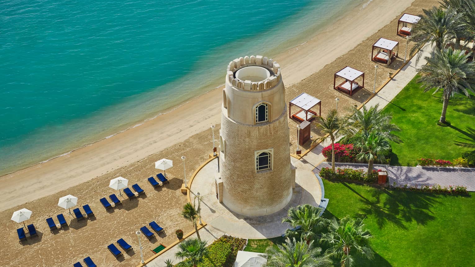 Aerial view of Four Seasons Hotel Doha beach with large tower by cabanas, chairs, umbrellas on sand