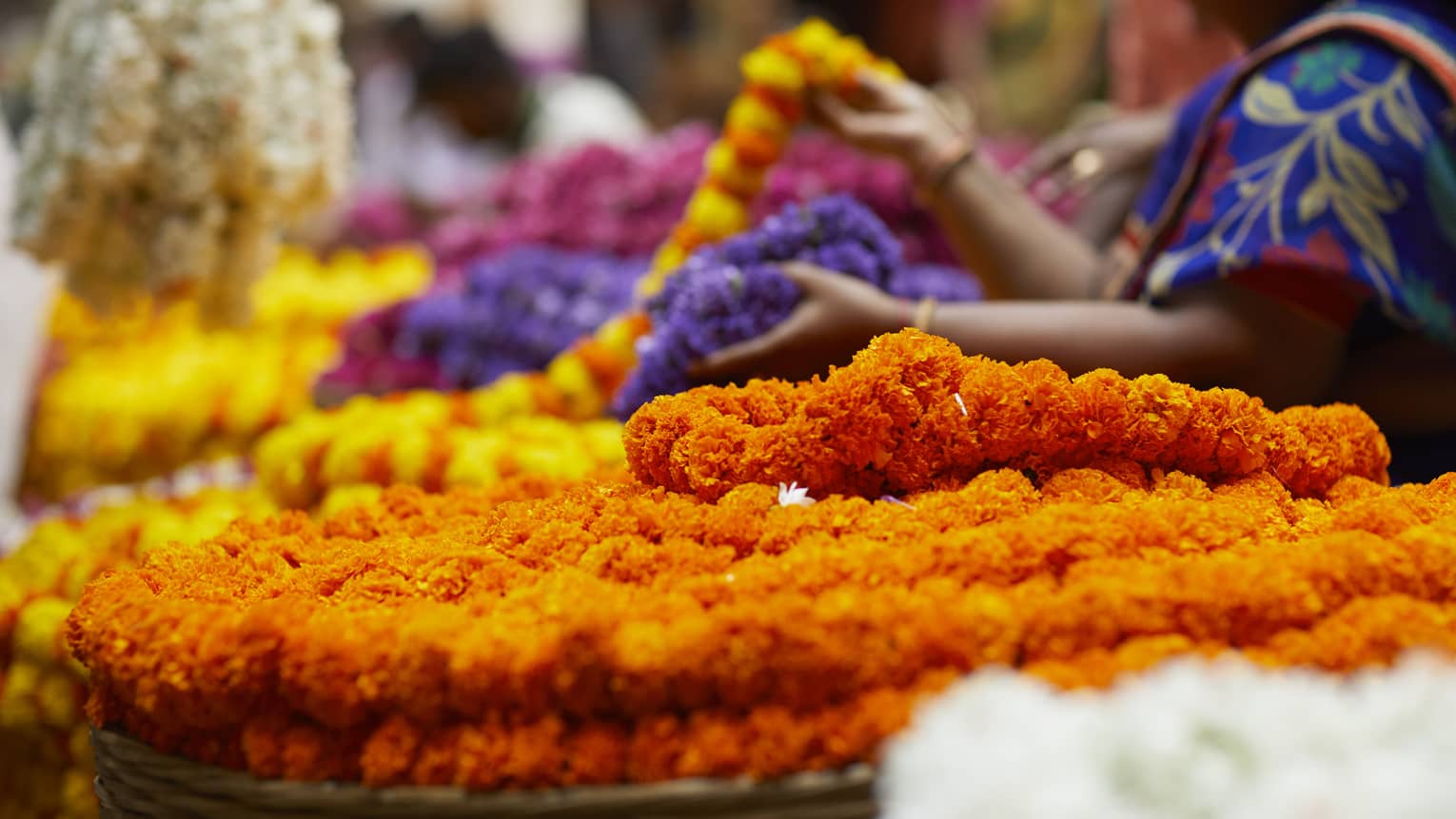 Close-up of vibrant chains of flowers amid a bustling market scene, where people sell and browse colourful floral displays.