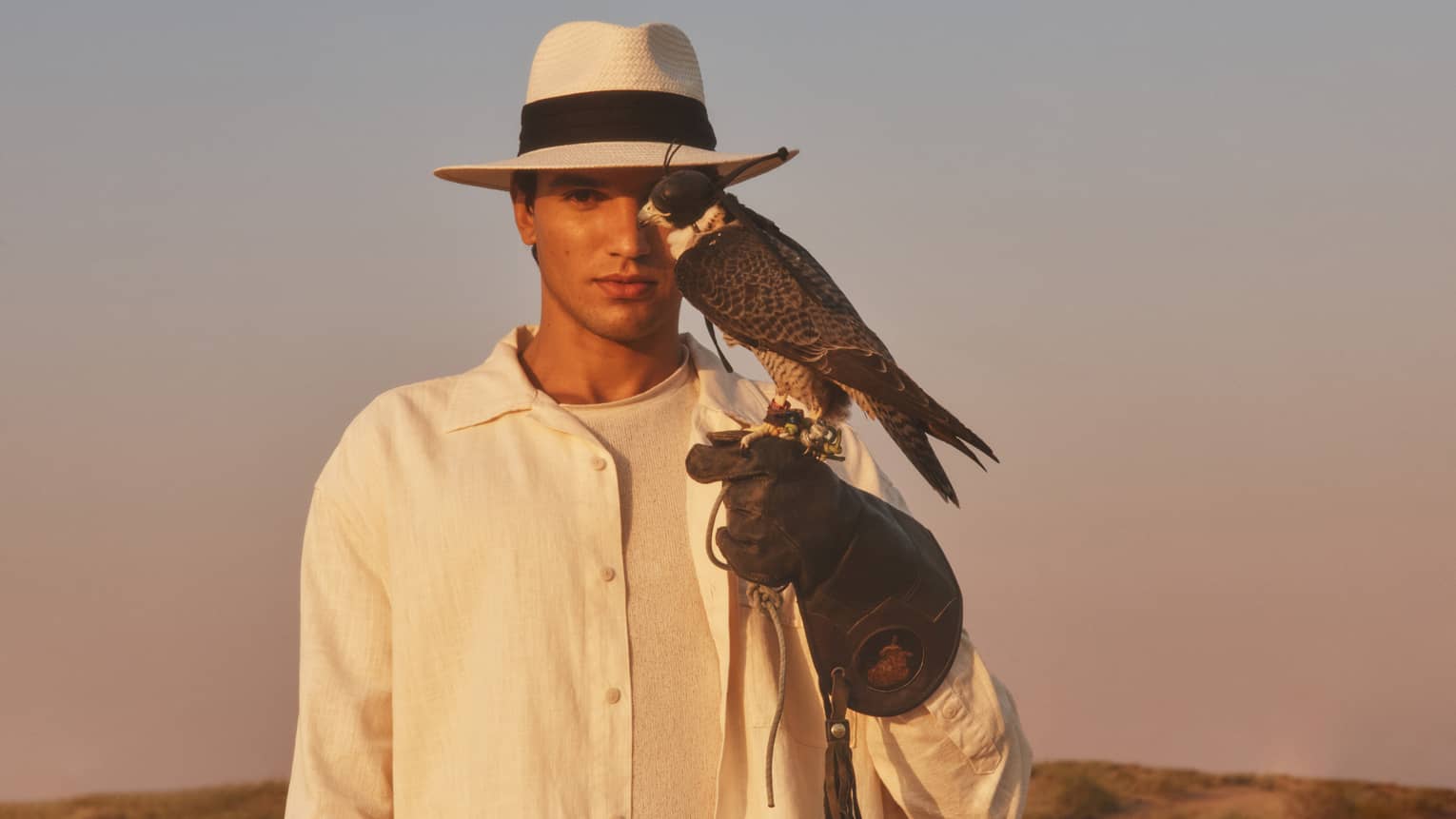 Person in straw hat and white shirt with gloved hand outstretched and hawk perched on it