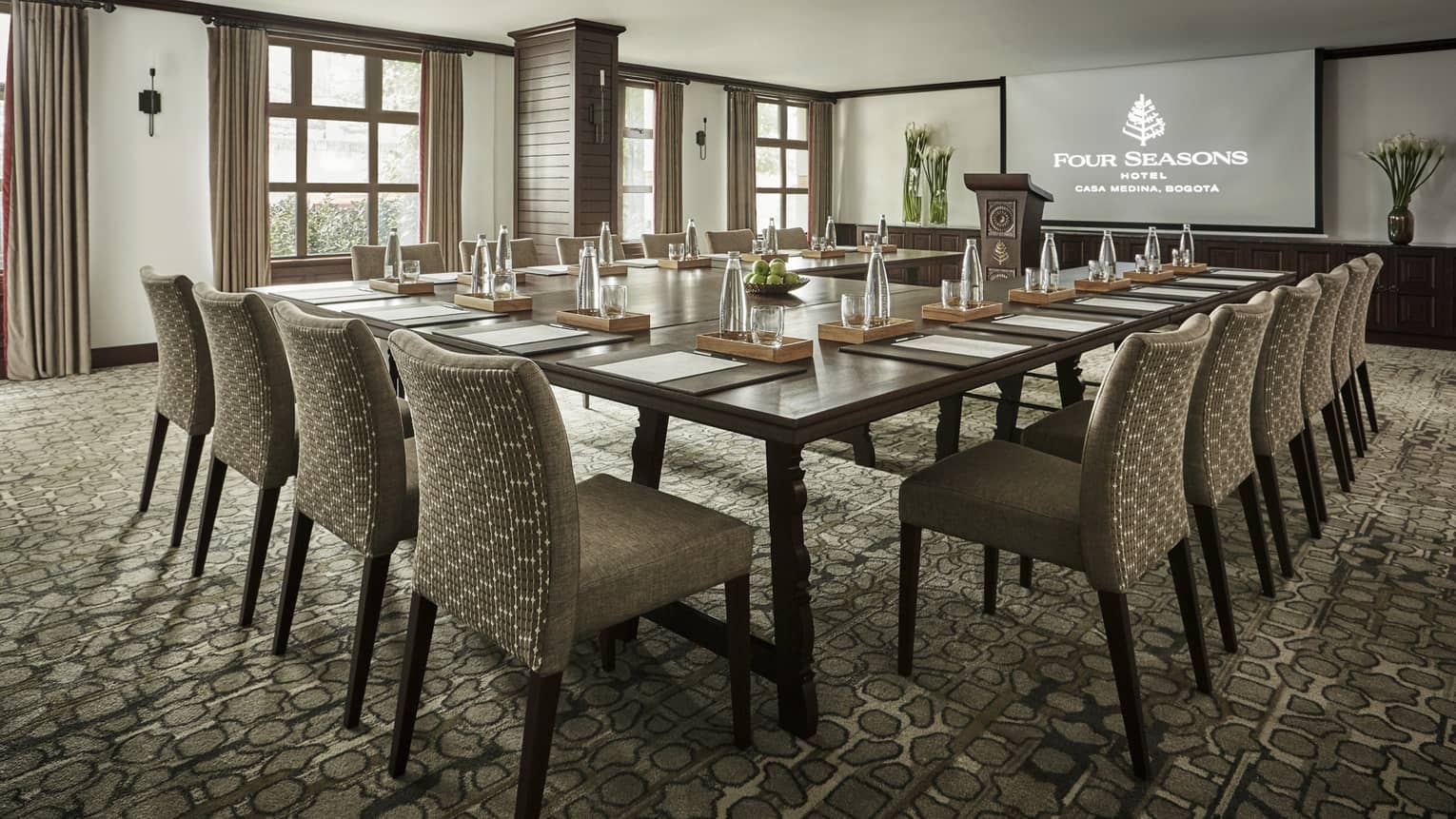 El Nogal meeting room with modular tables and chairs facing screen, wall of windows