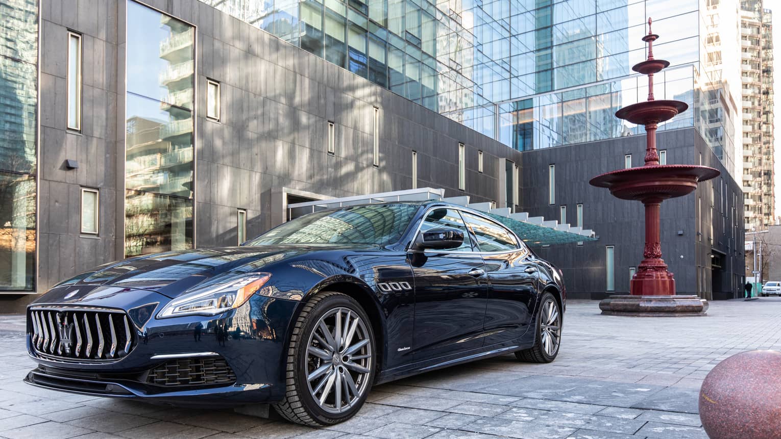 A dark blue Maserati is parked in front of hotel building
