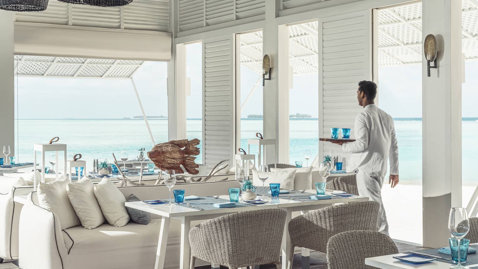 Waiter walks by tables with tray of water glasses at open-air Blu Beach Club