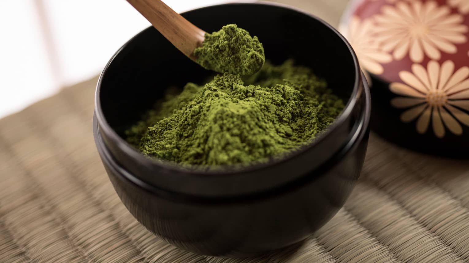 Close-up of green matcha tea powder in small black bowl, wood spoon