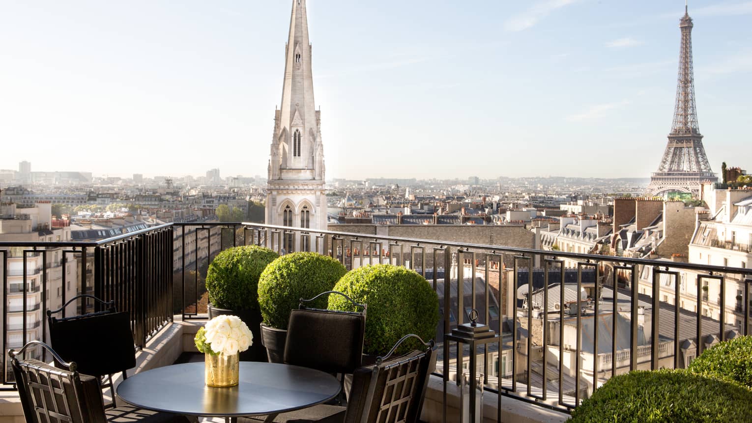 Patio dining table with white roses, potted shrubs iron balcony overlooking Paris rooftops, cathedrals