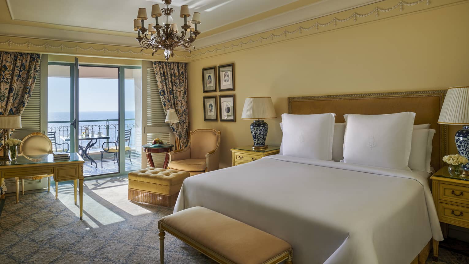 Elegant suite with vintage furniture, drapes framing window leading to balcony and sea views