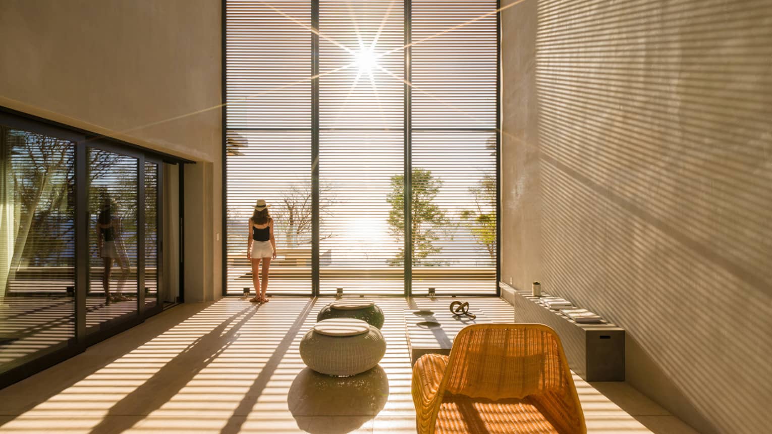 Woman stands by sunny floor to ceiling window in modern room