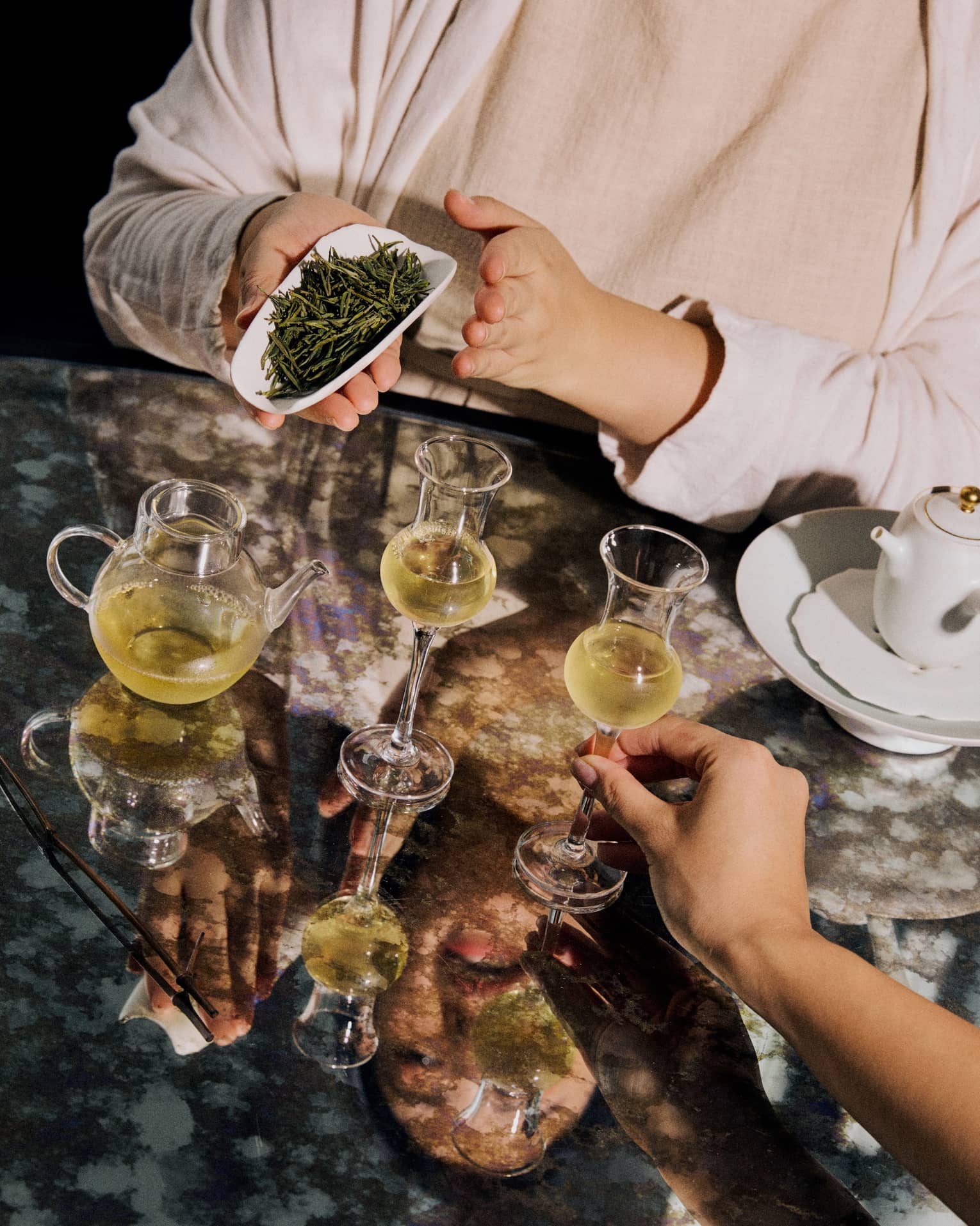 Loose leaf green tea displayed alongside two clear glasses of tea and a teapot.
