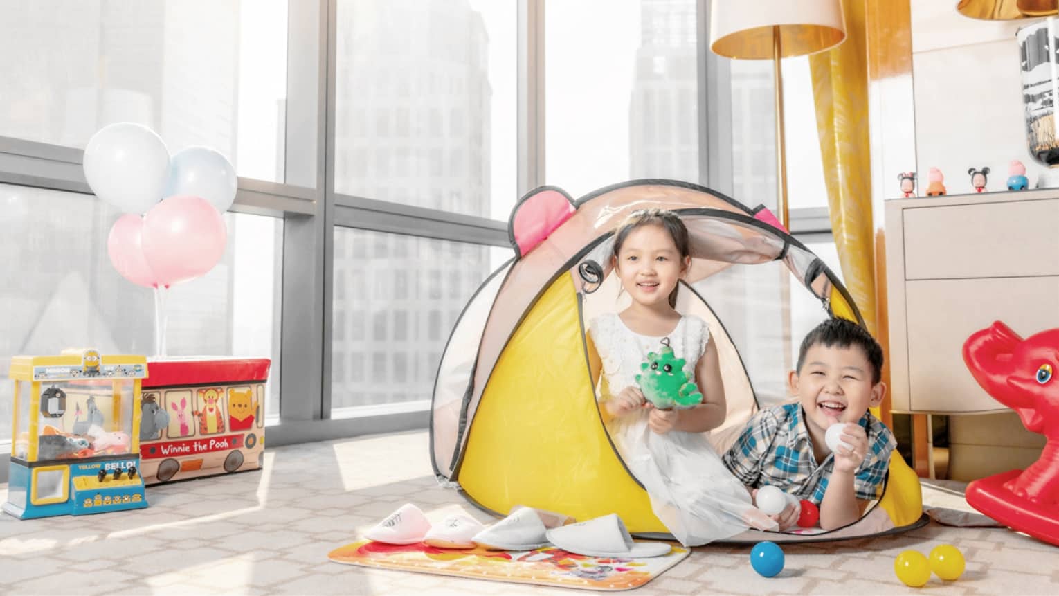 Two children play in a hotel room in Tianjin with windows facing the city