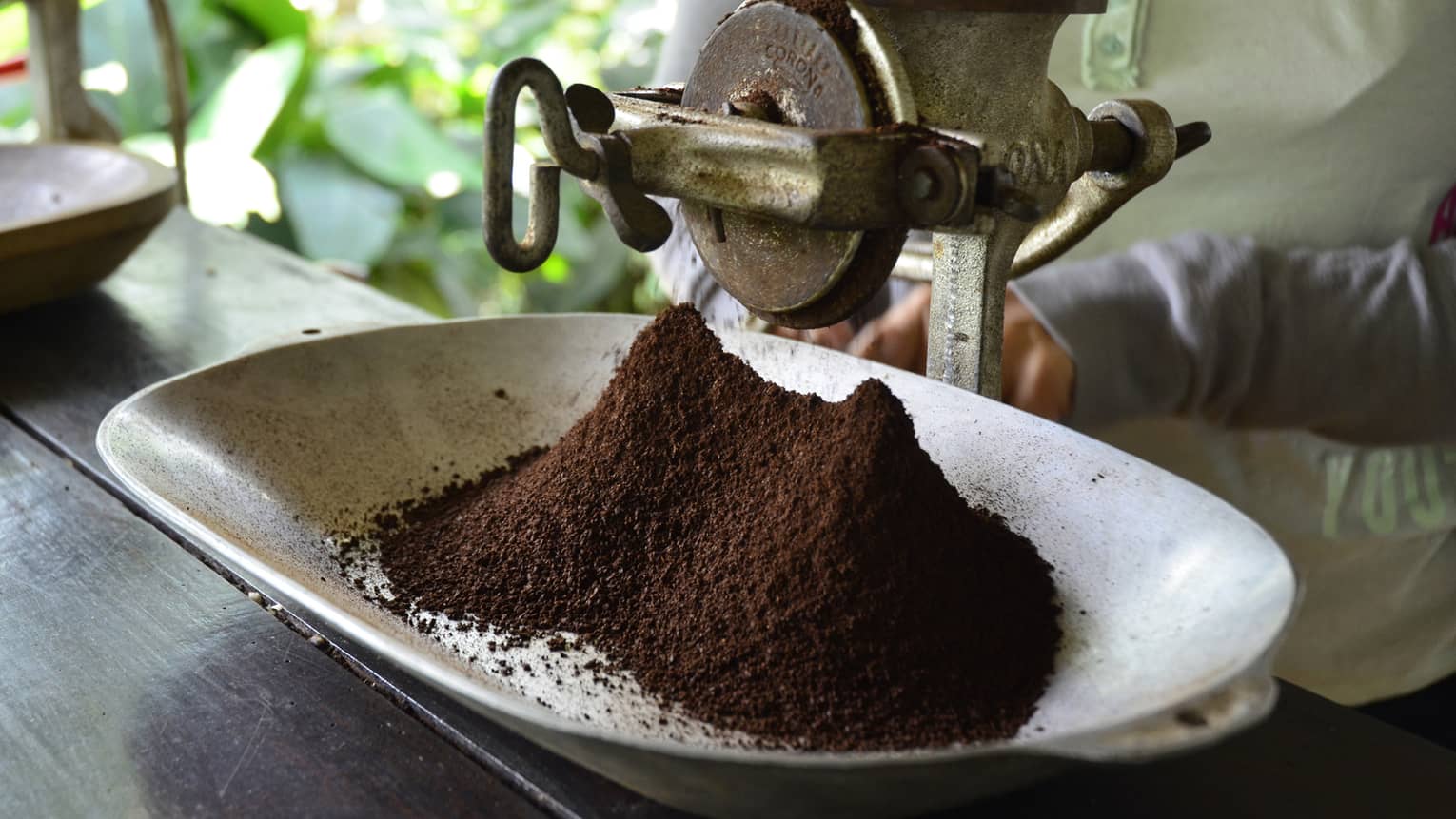 Large metal industrial-looking hand grinder with pile of ground Colombian coffee 