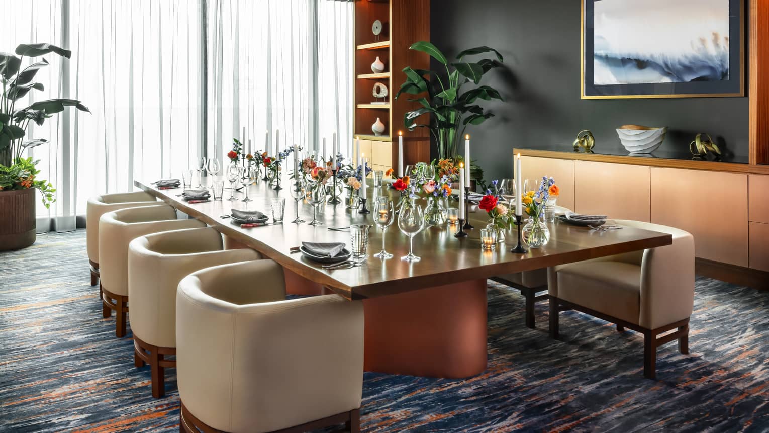 Dining table set with glasses and vases of flowers in a room with floor-to-ceiling windows