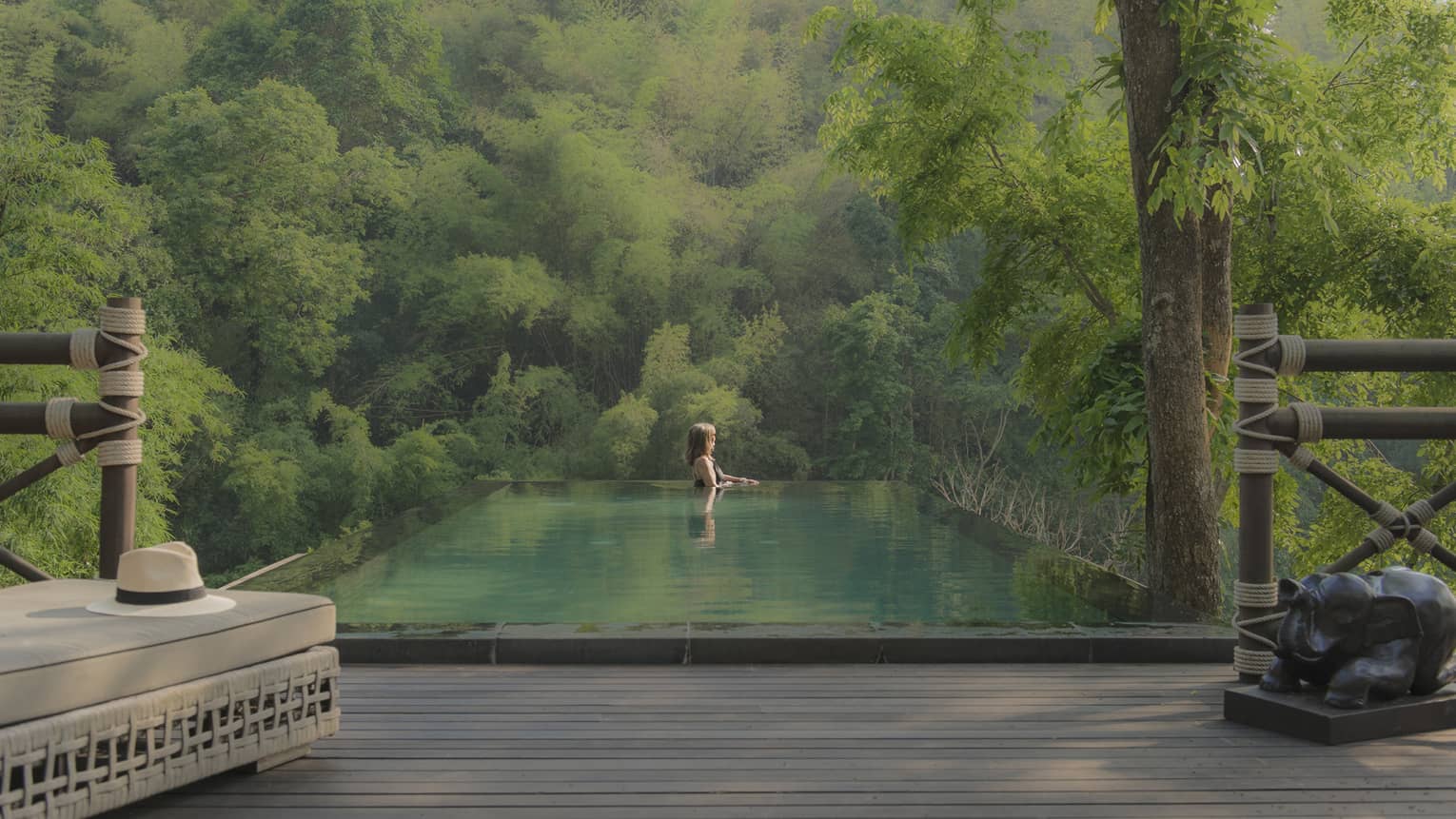 Woman in swimming pool at Four Seasons Tented Camp Golden Triangle, surrounded by green water with hillside jungle beyond