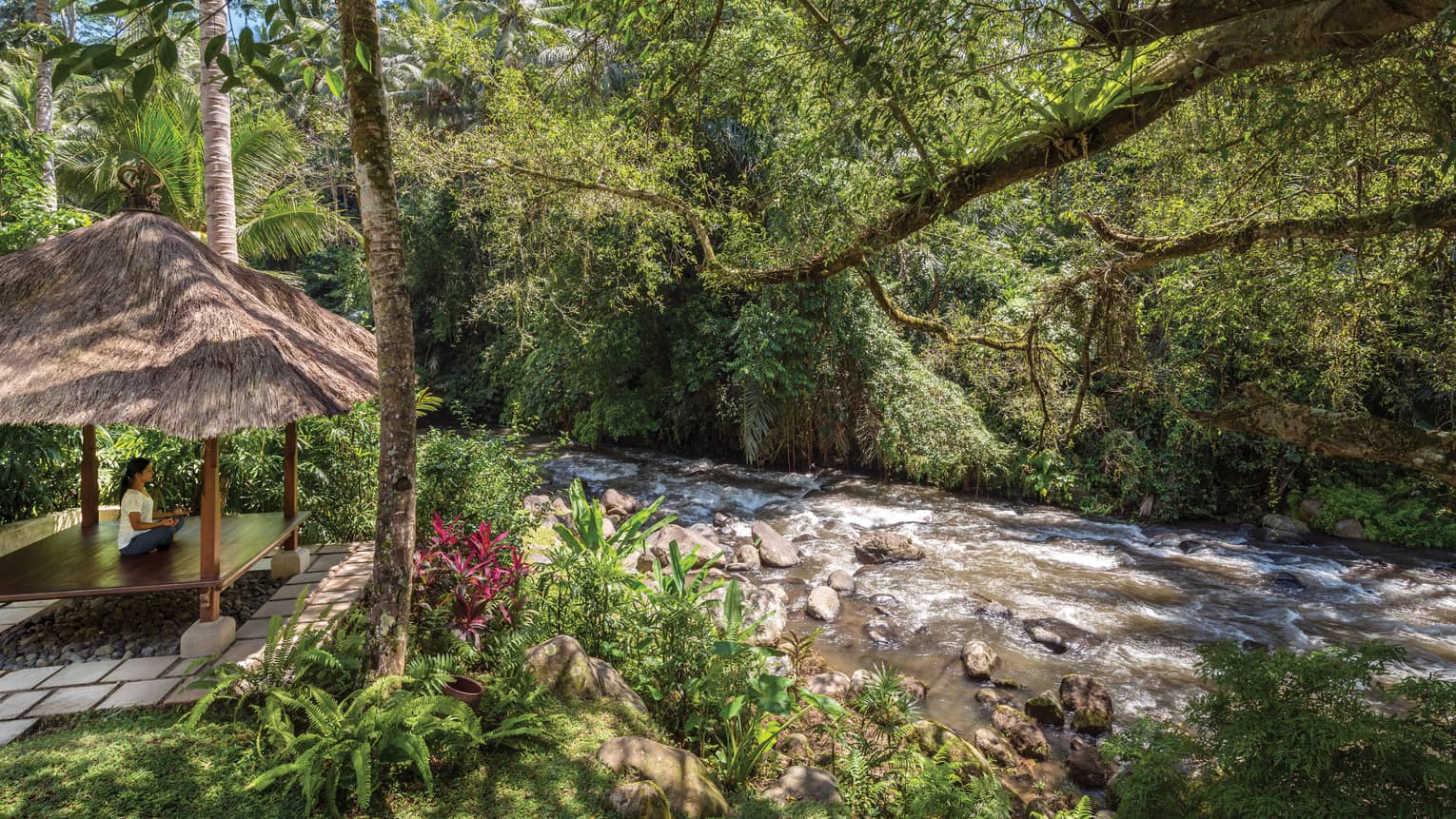 A guest meditating in a pavilion next to a flowing river in Bali