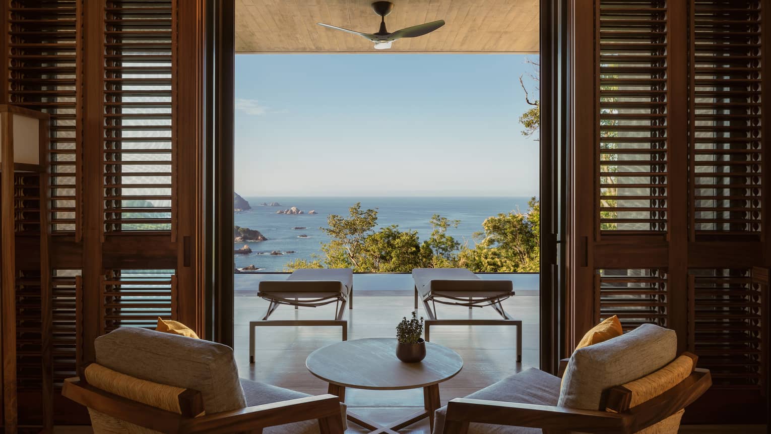Two arm chairs and small table face outwards to pool terrace, overlooking trees and ocean