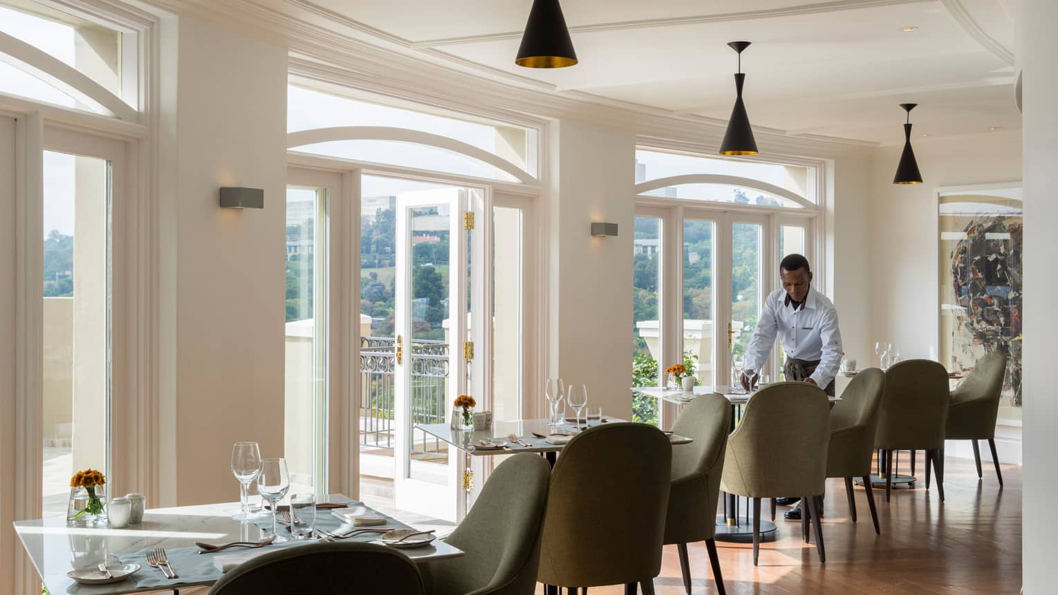 Waiter sets dining table in sunny Flames restaurant dining room
