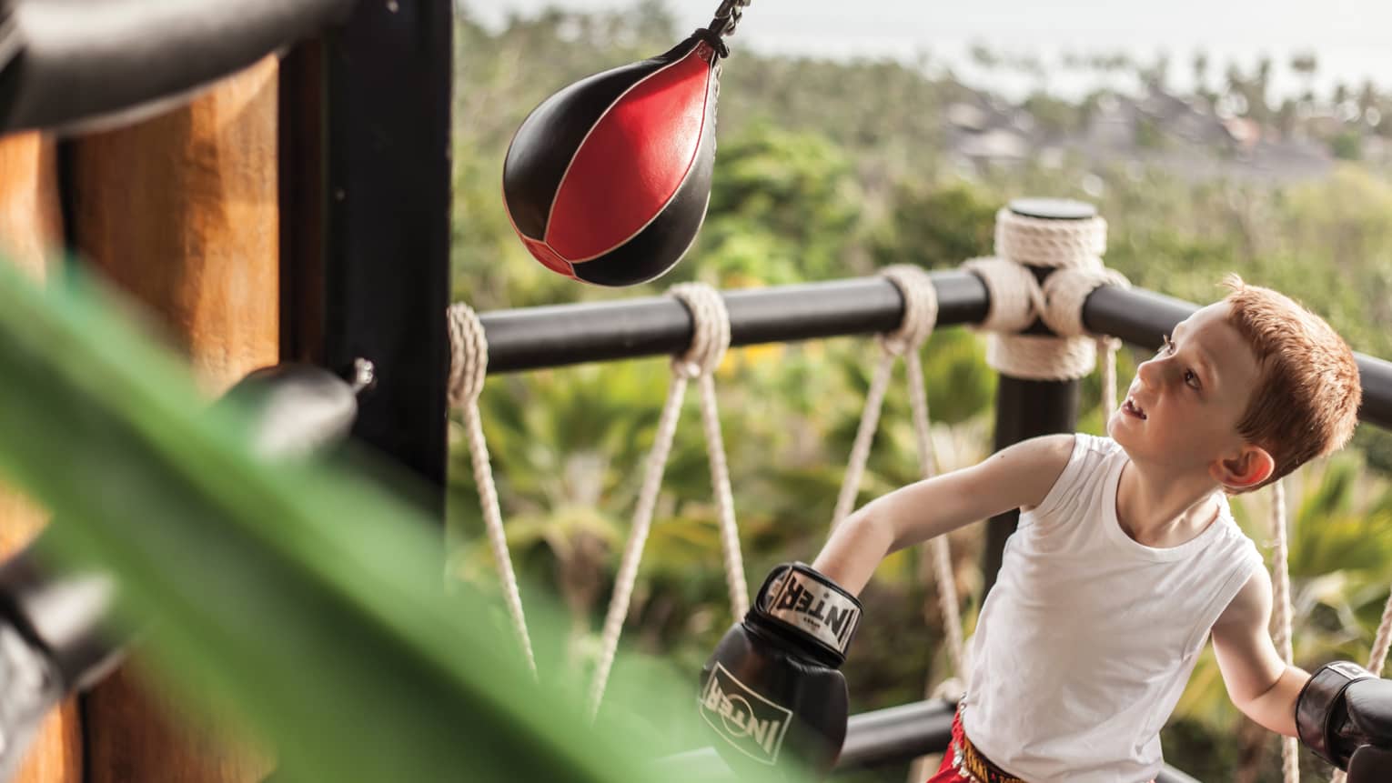 Young boy wearing boxing gloves in ring with small Muay Thai boxing bag