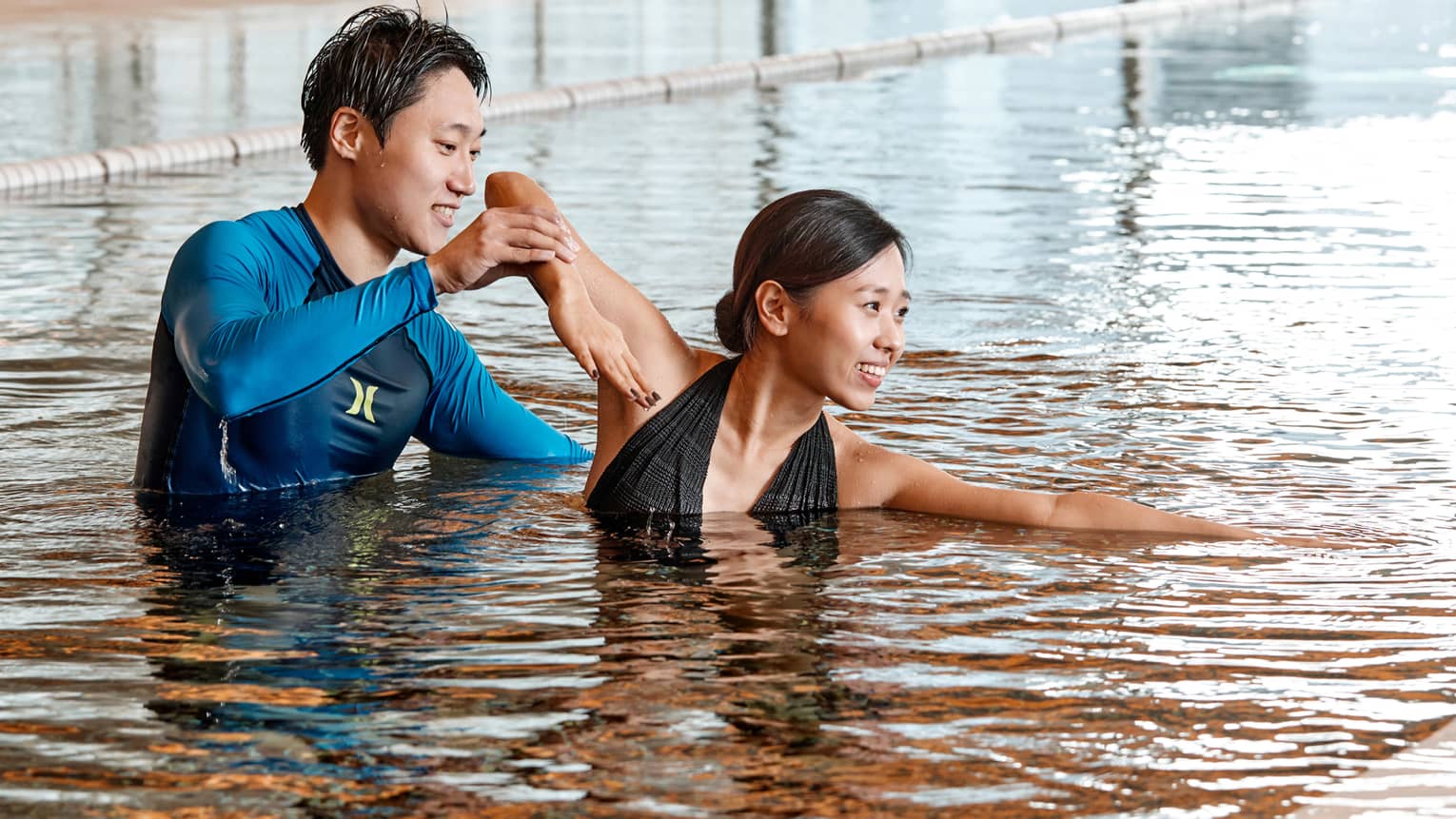 Swimming instructor helps woman position arm in indoor swimming pool