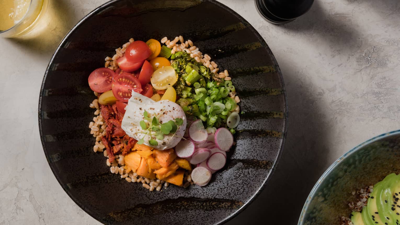 A black bowl of tomatoes, nuts, herbs, and vegetables.