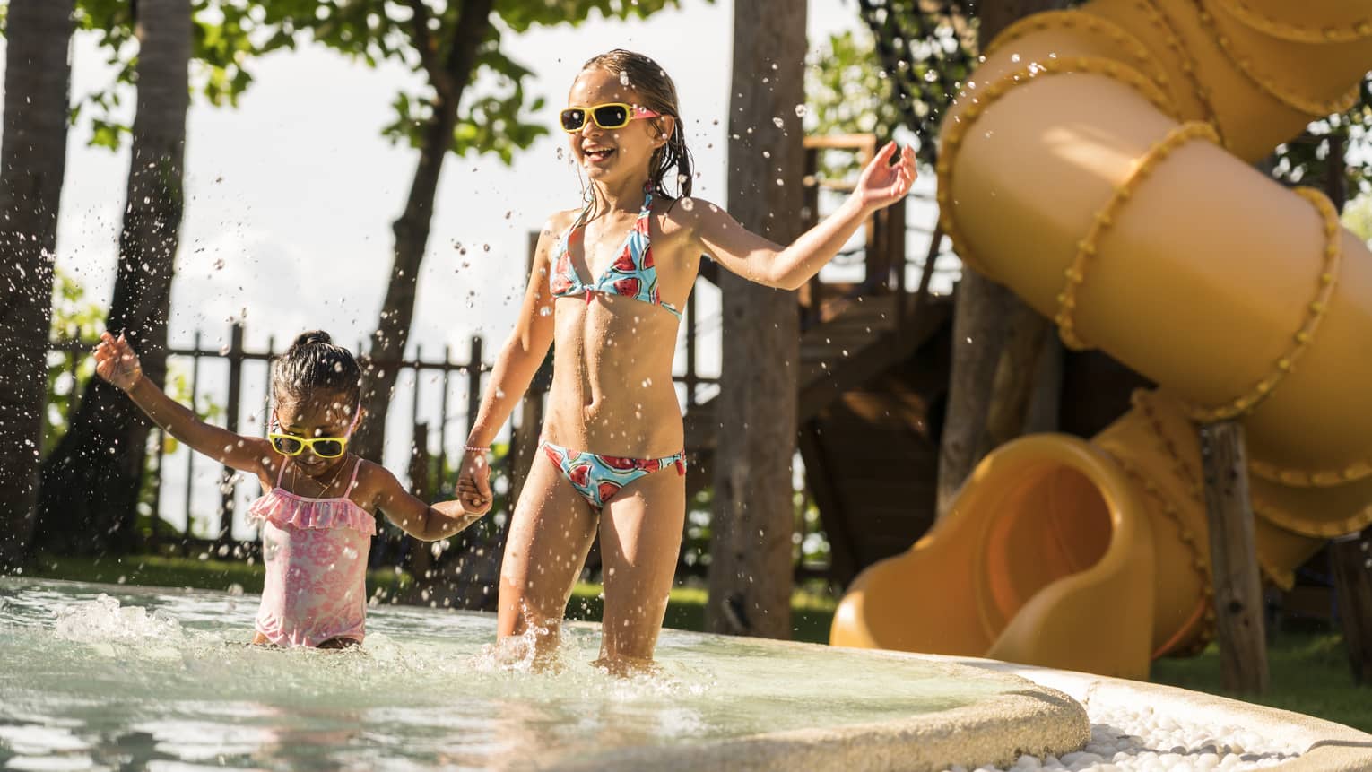 Two young girls splash in the kiddie pool, a water slide in the background