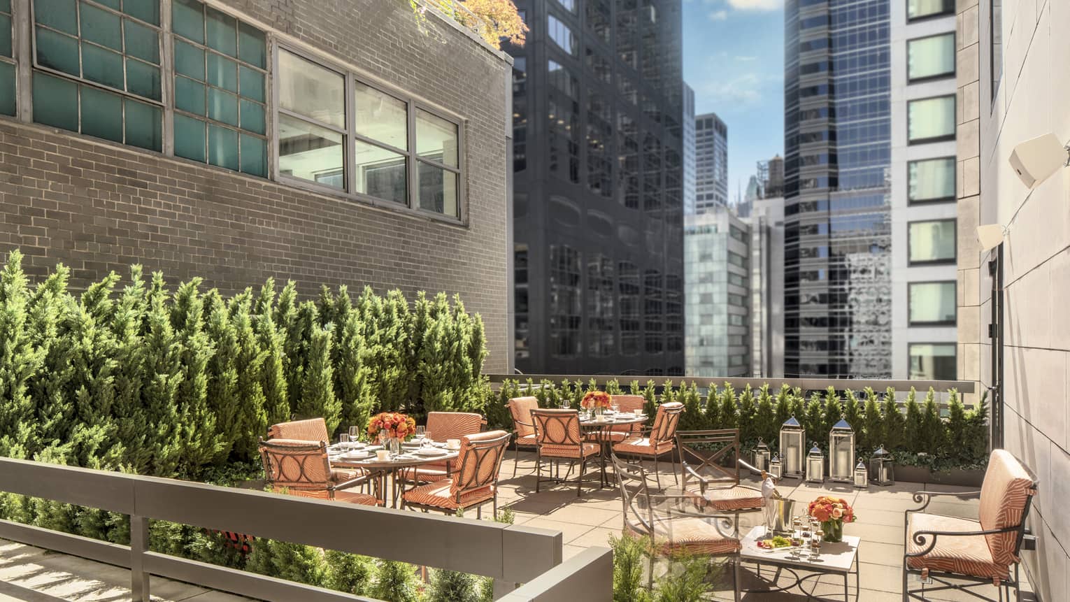 11th Floor Terrace Boardroom, surrounded by green topiaries, with square iron and glass tables with orange cushions on chairs at Four Seasons Hotel New York