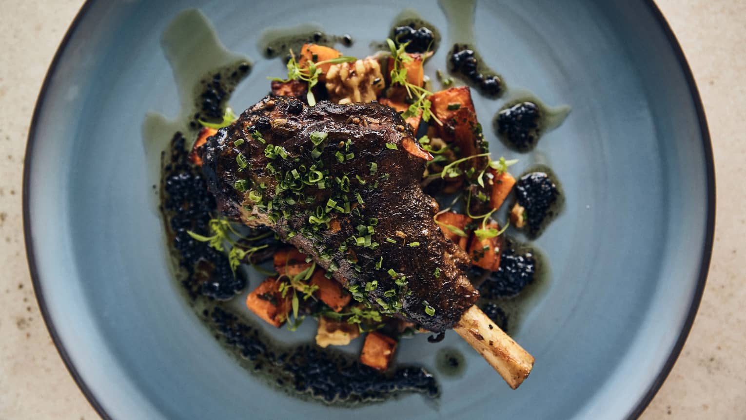 A steak with bone on a dark green sauce on a blue plate.